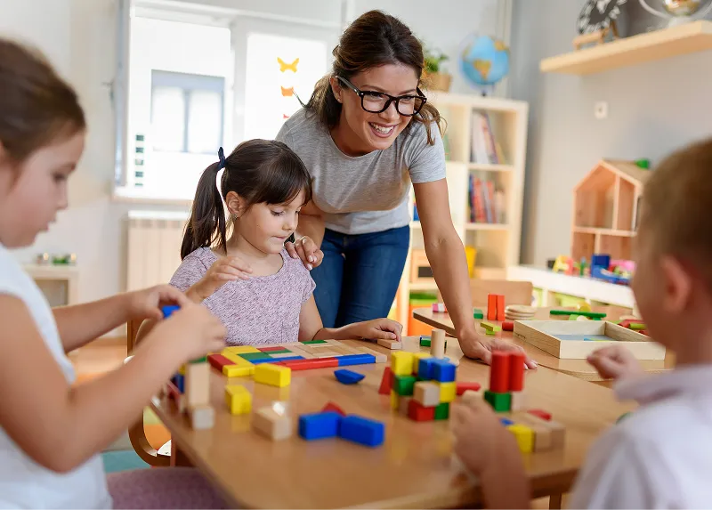 Un'educatrice sorridente gioca con i bambini ai tavoli del Centro Evolutivo
